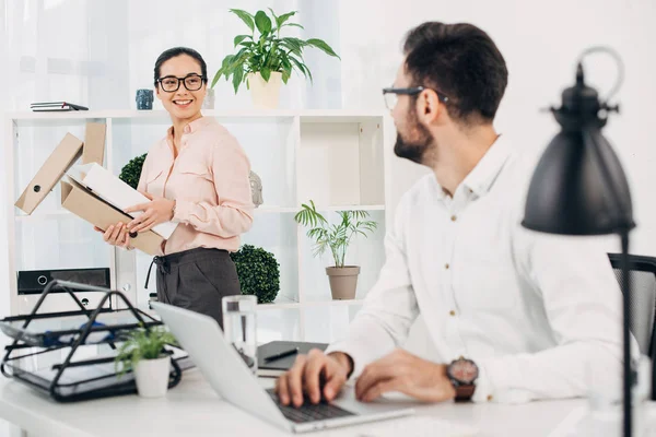 Selective focus of female manager standing with folders and looking at male coworker — Stock Photo