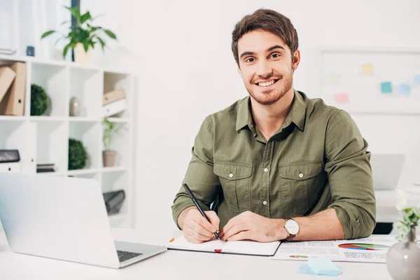 Joven empresario sonriendo y sosteniendo la pluma en la oficina moderna - foto de stock