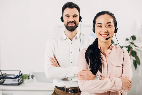 Focus selettivo del manager femminile sorridente con le braccia incrociate mentre il collega di lavoro maschile in piedi dietro con auricolare — Foto stock