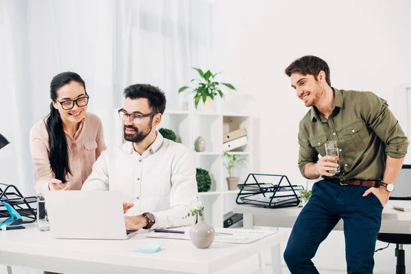 Junger Manager steht mit einem Glas Wasser und blickt auf Mitarbeiter im Büro — Stockfoto