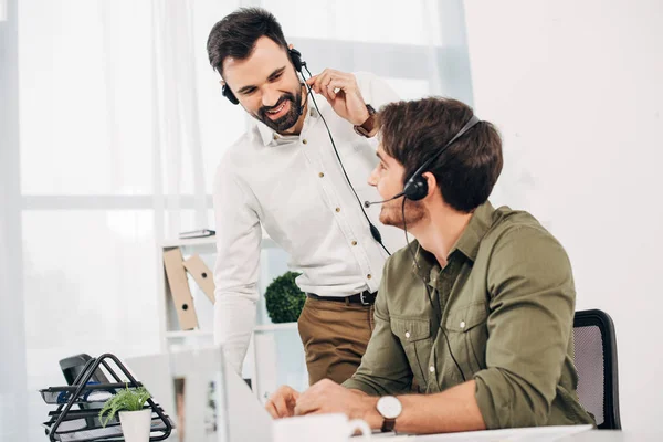 Operatore sorridente che guarda il collega in cuffia nel moderno call center — Foto stock