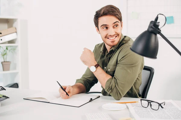 Веселый бизнесмен улыбается с ручкой в руке в офисе — стоковое фото