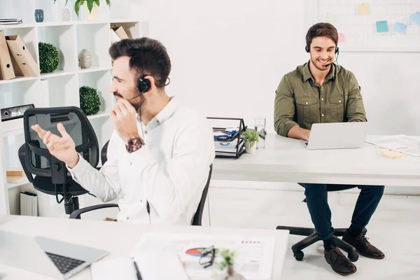 Operatori maschili che utilizzano cuffie mentre lavorano in un call center moderno — Foto stock