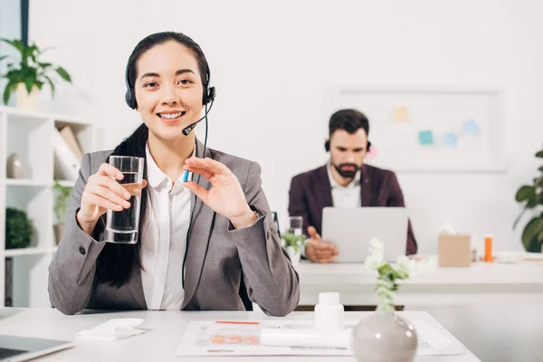 Focus selettivo del manager sorridente che tiene la pillola mentre il collega di sesso maschile sullo sfondo — Foto stock