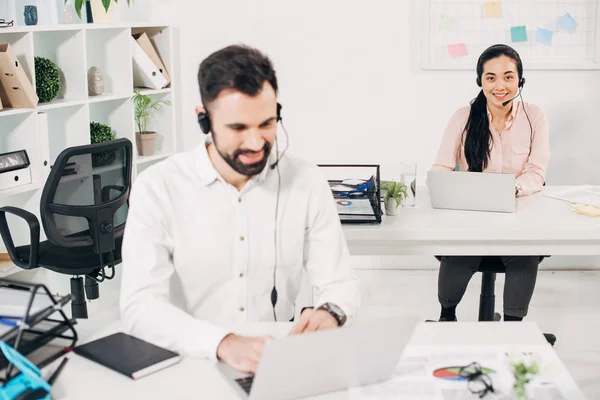 Selective focus of female manager sitting in headset near male coworker in office — Stock Photo