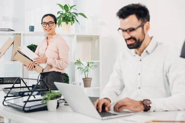 Female manager standing with folders while male coworker typing at laptop keyboard — Stock Photo