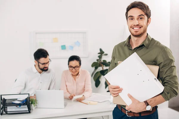 Selective focus of young manager standing with folders in office — Stock Photo