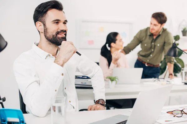 Thoughtful office manager sitting in office with coworkers on background — Stock Photo