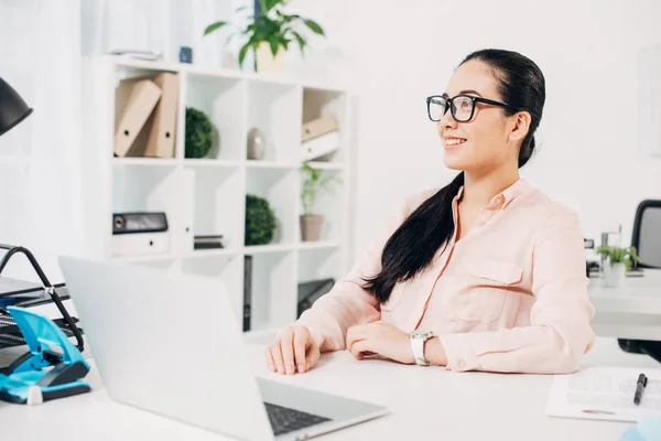 Hermosa mujer de negocios sentada y sonriendo en el escritorio con computadora portátil - foto de stock