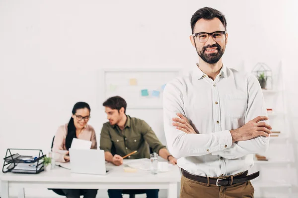 Selective focus of manager standing with crossed arms with coworkers on background — Stock Photo