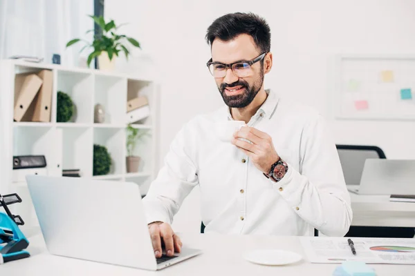 Empresário bebendo café e olhando para laptop no escritório — Fotografia de Stock