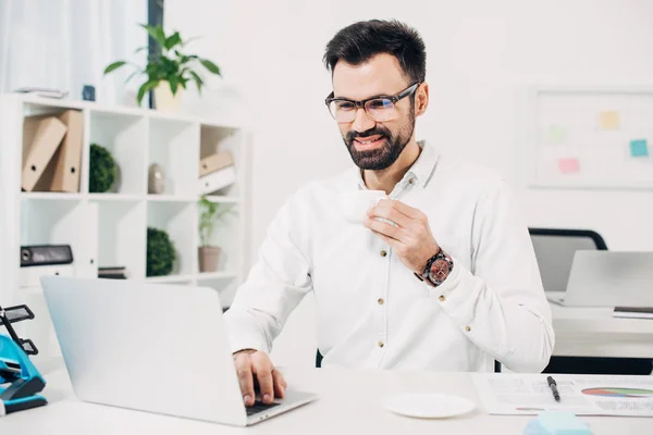 Empresario bebiendo café y mirando el portátil en la oficina - foto de stock