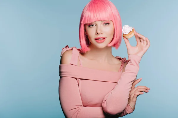 Красивая счастливая девушка в розовом парике позирует с вкусным кексом изолированы на синий — стоковое фото