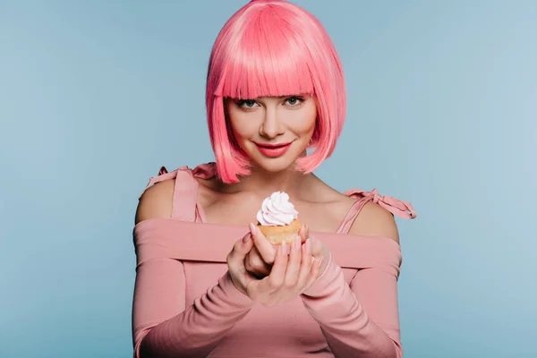 Chica sonriente con el pelo rosa sosteniendo sabroso cupcake aislado en azul - foto de stock
