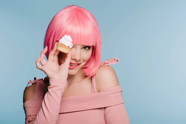 Attraktive lächelnde Mädchen in rosa Perücke hält Cupcake isoliert auf blau — Stockfoto