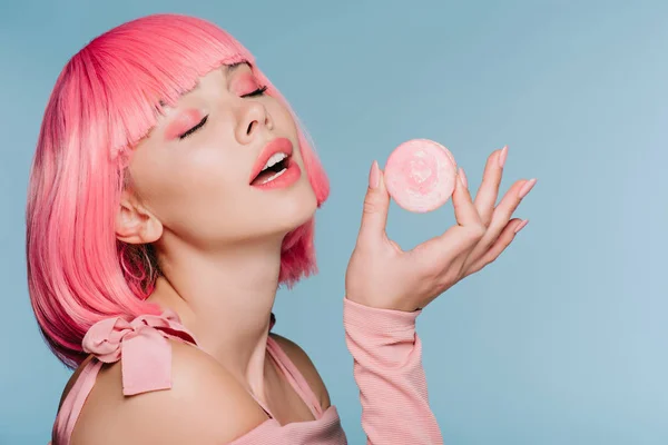 Seductora chica de peluca rosa posando con macaron aislado en azul - foto de stock