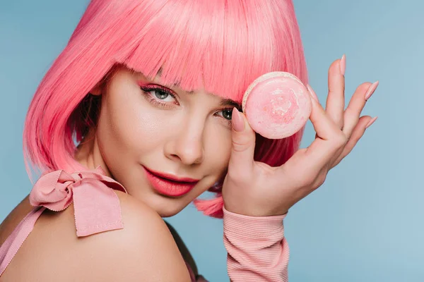 Attraktive junge Frau in pinkfarbener Perücke posiert mit Makkaron auf blauem Grund — Stockfoto