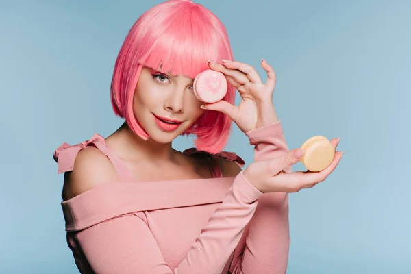 Chica de moda en peluca rosa posando con dos macarrones aislados en azul - foto de stock
