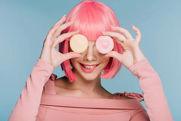 Attraente sorridente ragazza in parrucca rosa in posa con due macaron isolati su blu — Foto stock