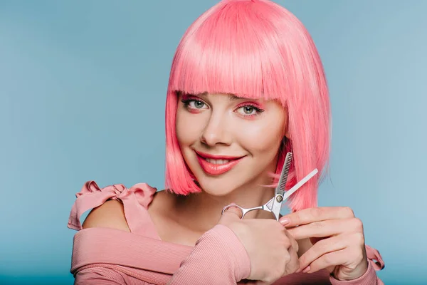 Усміхнена модна дівчина, що ріже рожеве волосся з ножицями ізольовано на синьому — стокове фото