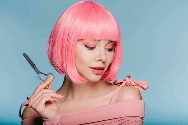 Hermosa chica con estilo en rosa peluca sosteniendo tijeras aisladas en azul - foto de stock