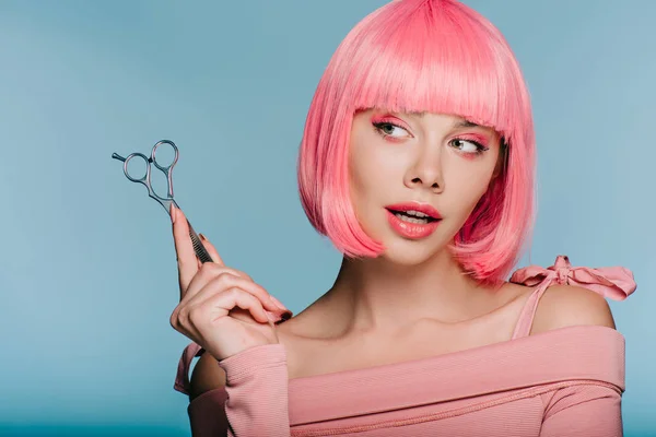 Atractiva chica sensual en peluca rosa sosteniendo tijeras aisladas en azul - foto de stock