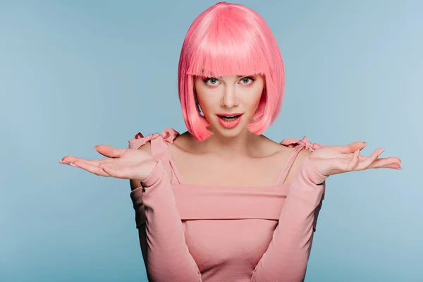 Fashionable shocked girl in pink wig posing with shrug gesture isolated on blue — Stock Photo