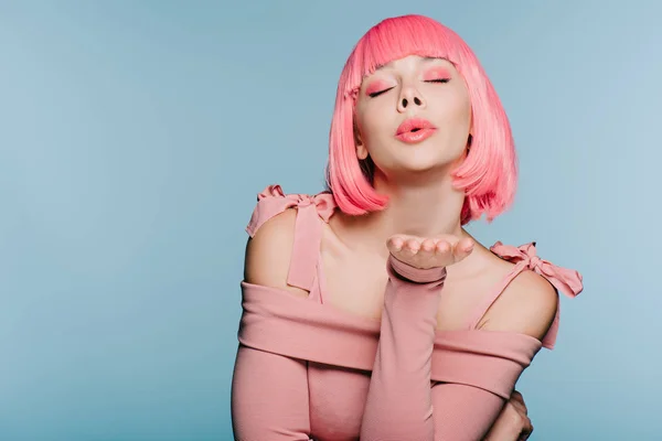 Chica de moda en rosa peluca soplado aire beso con los ojos cerrados aislado en azul - foto de stock
