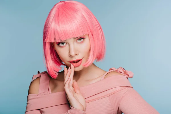 Überraschte junge Frau gestikuliert und posiert in pinkfarbener Perücke auf blauem Grund — Stockfoto