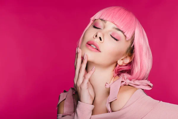 Tierna mujer joven con estilo en peluca rosa posando con los ojos cerrados, aislado en rosa - foto de stock