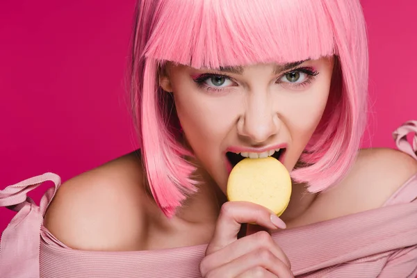 Attraente ragazza aggressiva in parrucca rosa mordente macaron isolato su rosa — Foto stock