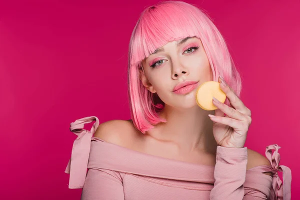 Belle femme en perruque rose posant avec macaron isolé sur rose — Photo de stock