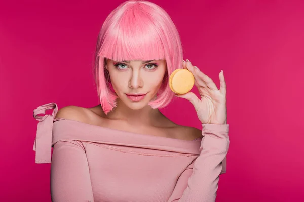 Hermosa chica en rosa peluca posando con dulce macaron aislado en rosa - foto de stock