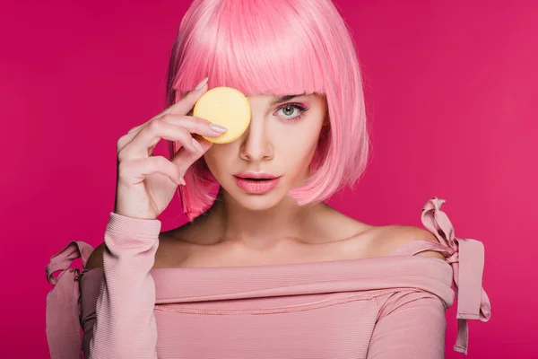 Joven mujer de moda en peluca rosa posando con macaron aislado en rosa - foto de stock