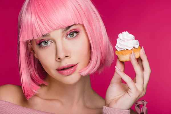Hermosa chica en rosa peluca celebración delicioso cupcake aislado en rosa - foto de stock