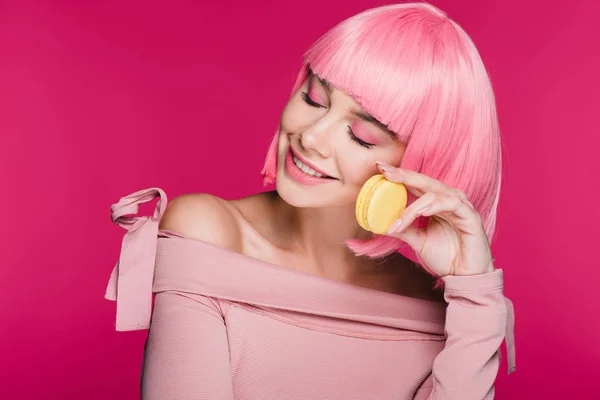 Donna sognante sorridente in parrucca rosa in posa con macaron isolato su rosa — Foto stock