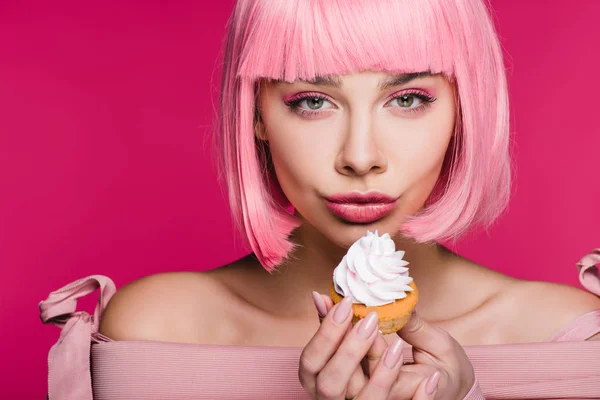 Menina atraente em peruca rosa segurando delicioso cupcake com creme de manteiga isolado em rosa — Fotografia de Stock