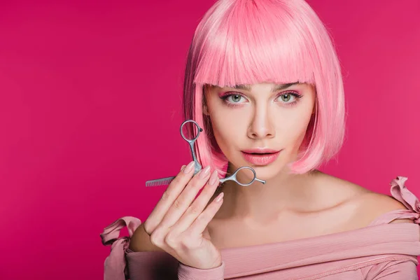 Hermosa chica con estilo en rosa peluca sosteniendo tijeras aisladas en rosa - foto de stock