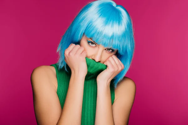 Attractive girl with blue hair hiding face in green turtleneck, isolated on pink — Stock Photo