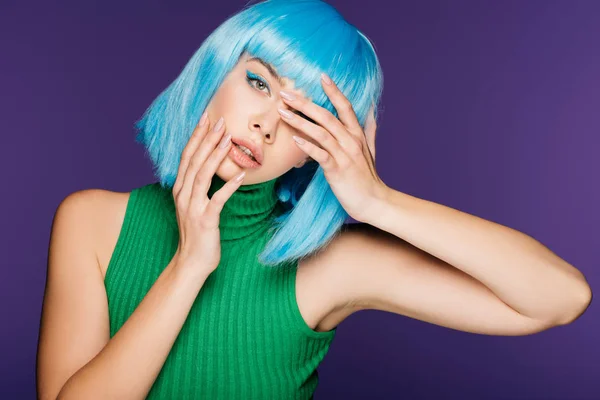 Atractiva chica sensual gesto y posando en peluca azul, aislado en púrpura - foto de stock
