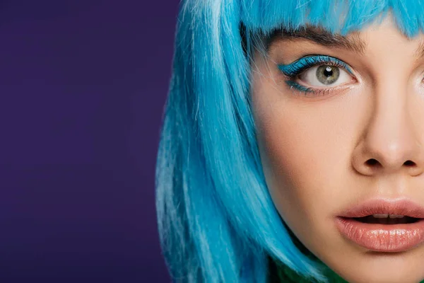 Обрезанный вид привлекательной девушки с голубым макияжем позируя в голубом парике, изолированные на фиолетовый — стоковое фото