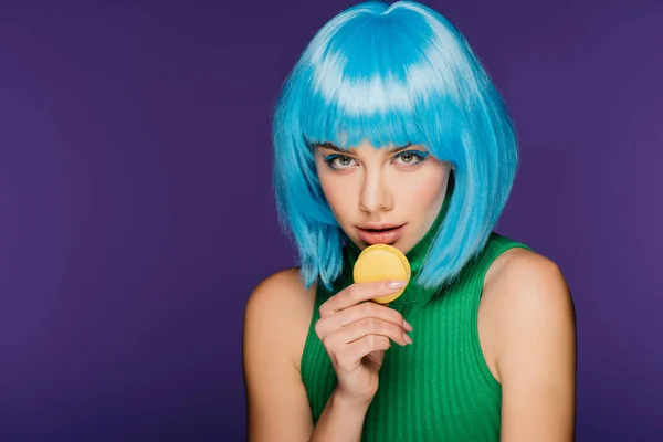 Hermosa sensual chica en azul peluca posando con dulce sabroso macaron aislado en púrpura - foto de stock