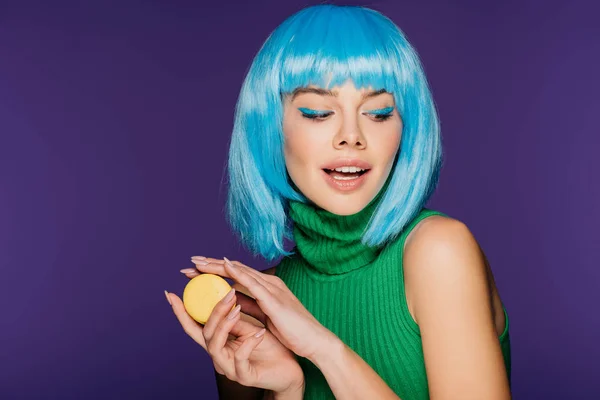 Elegante chica sensual en peluca azul posando con macaron aislado en púrpura - foto de stock