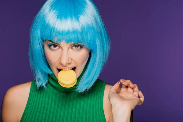 Attractive sensual woman in blue wig biting macaron isolated on purple — Stock Photo