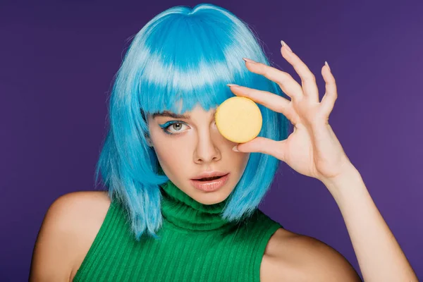 Atractiva chica sensual en peluca azul posando con macaron aislado en púrpura - foto de stock