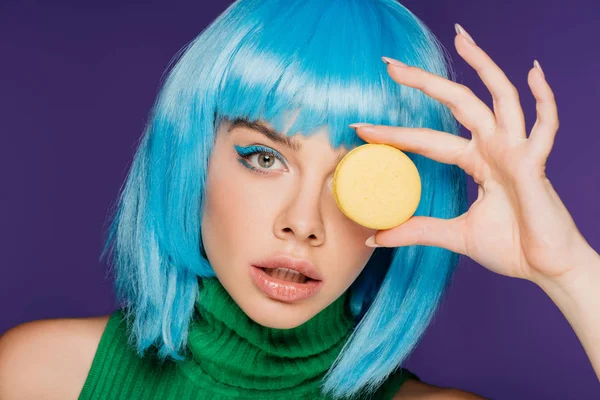 Bella ragazza in parrucca blu in posa con dolce macaron isolato su viola — Foto stock