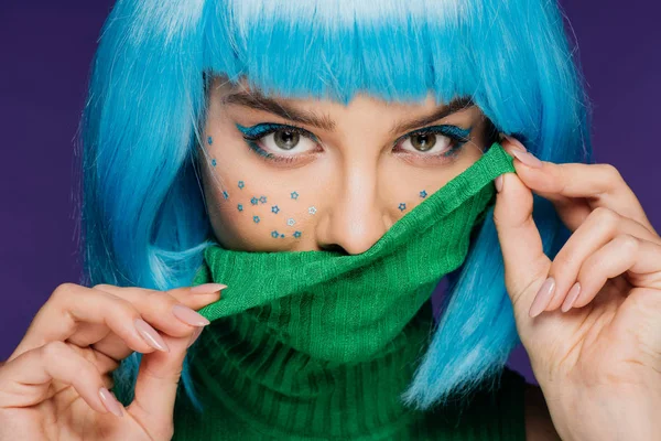 Atractiva chica de moda con peluca azul y estrellas en la cara posando con cuello alto verde, aislado en púrpura - foto de stock