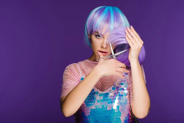 Приваблива молода жінка з зірками на обличчі, що ріже фіолетове волосся з ножицями, ізольована на фіолетовому — стокове фото