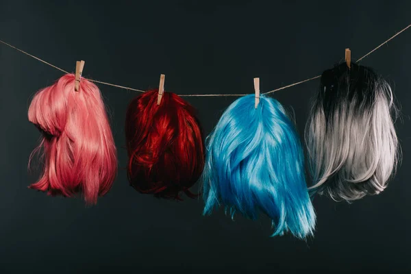 Four colorful wigs hanging on rope isolated on black — Stock Photo