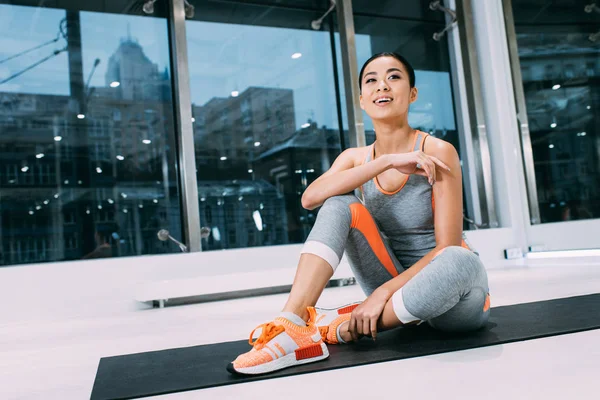 Приваблива азіатська спортсменка сидить на килимку і посміхається в спортзалі — стокове фото